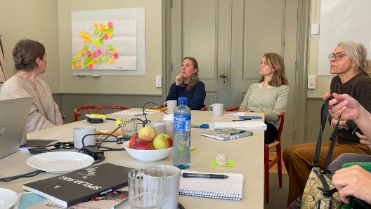 Flera personer sitter runt ett bord och diskuterar under en workshop.