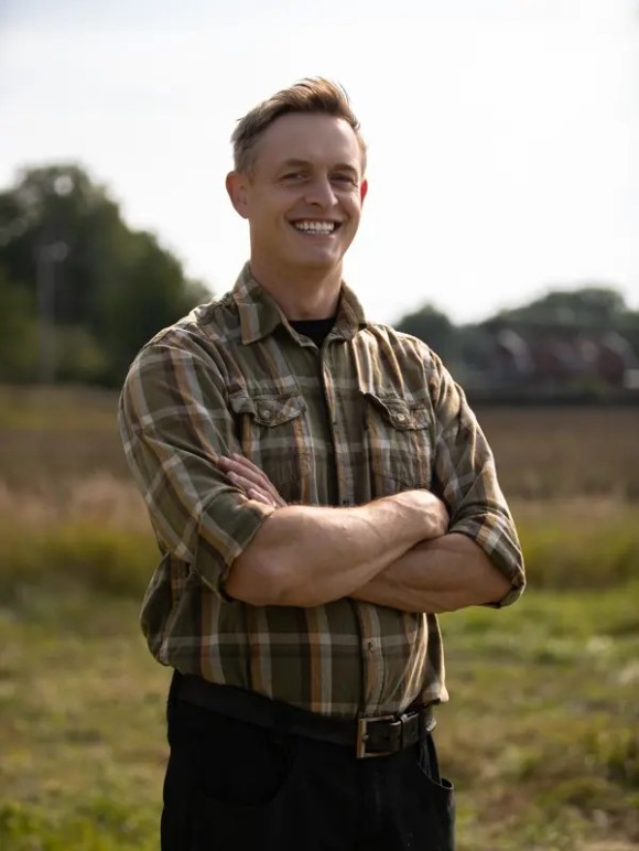 Glad ung man står med armarna i kors utomhus och tittar in i kameran