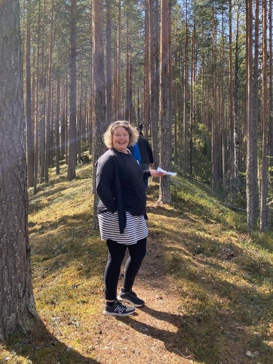 En person står på en sig omgiven av höga tallar. Solen skiner igenom tallarna. Foto Eva Sandberg