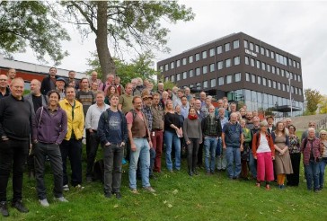 En stor samling människor som står i en grässlänt utanför ett stort hus