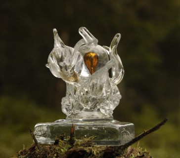 En statyett i glas i form av organiska "blad" omslutande en kula med glas som hyser en bronsfärgad bubbla.