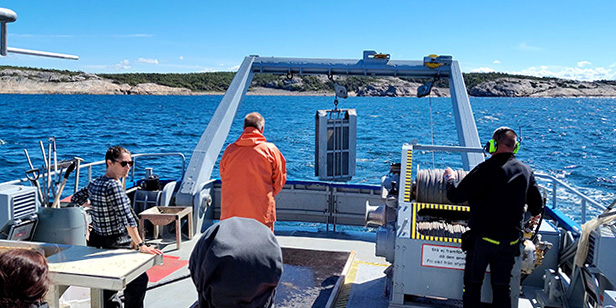 Öppen fiskebåt med arbetsklädda män ombord ute på solglittrande hav. Foto