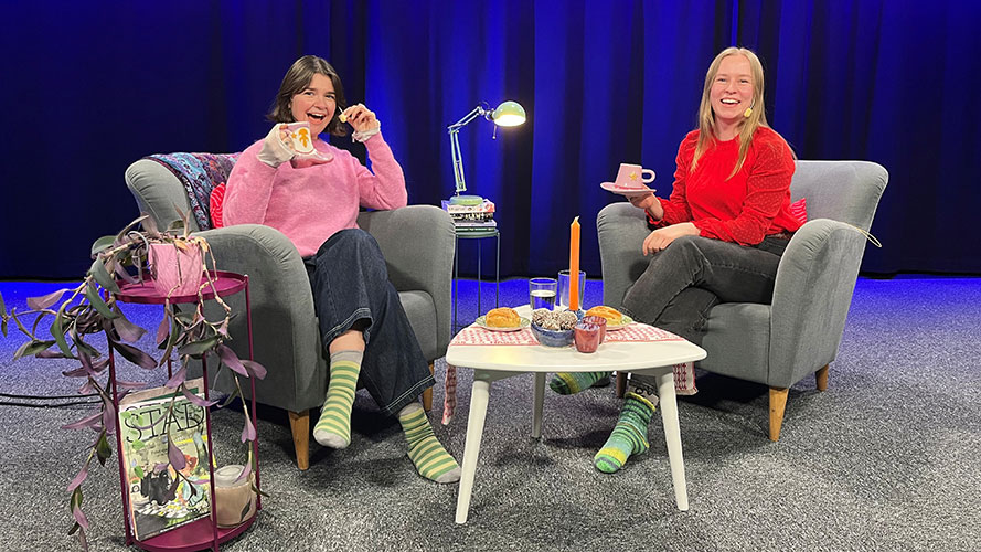 Two young women are sitting in a studio, each in their own armchair, chatting and drinking coffee.