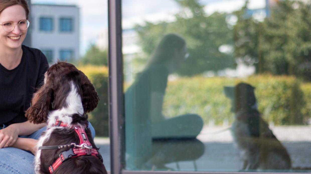 A woman and a dog with their reflections in a window. Photo.