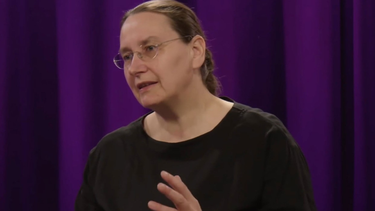 A woman in a studio in front of a purple curtain. Photo.