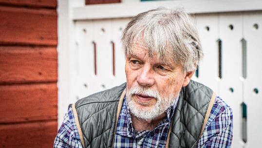 A man in front of a red and white wooden house. Photo.
