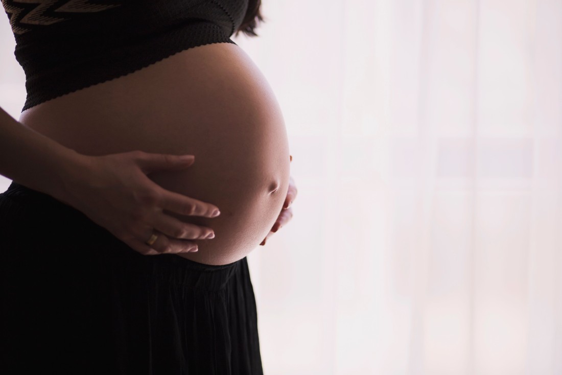A close-up of a pregnant woman touching her bare belly. Photo.