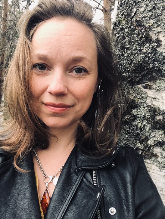 A woman with a black leather jacket in front of a birch tree. Photo.