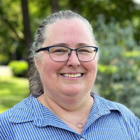 A headshot of a woman with glasses and a blue and white striped shirt.