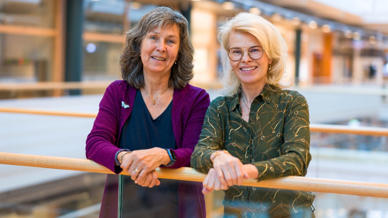 Two smiliing women by a railing. Photo. 