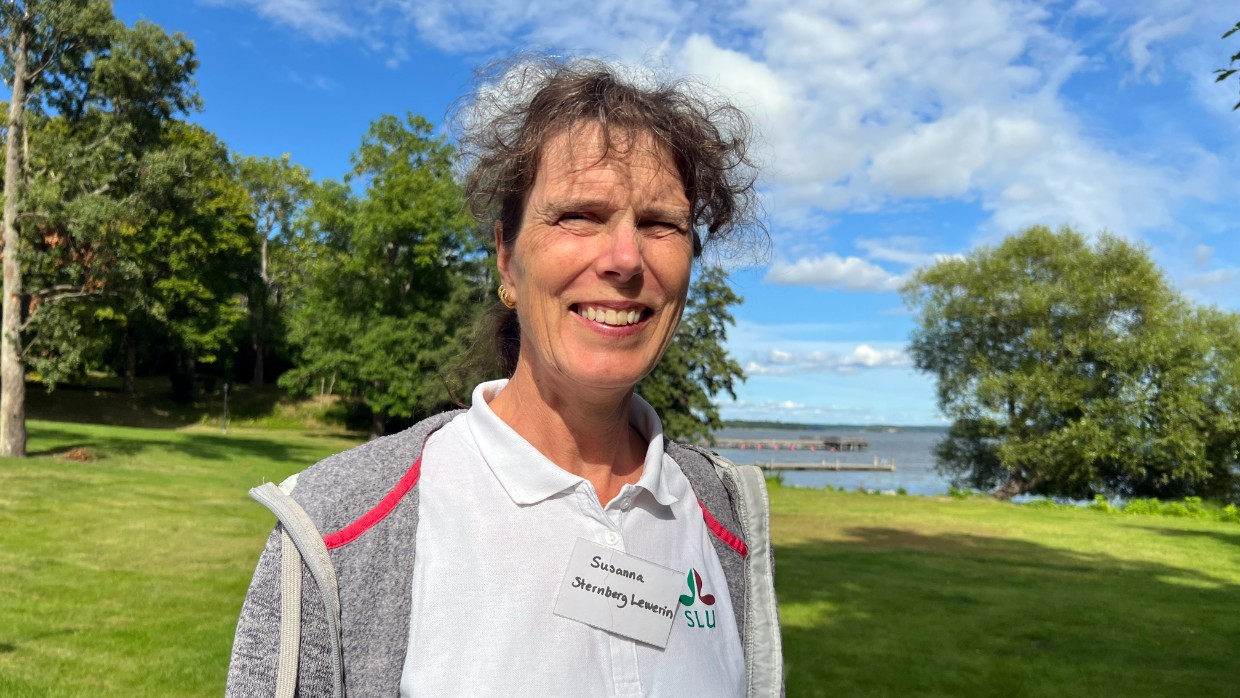 A woman with curly hair stands in sunlight with a lake in the background. Photo.