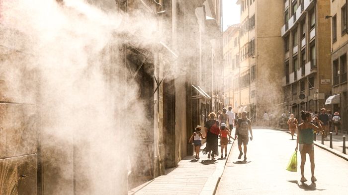 Summer street scene in Firenze, Italy, during a heatwave. People walking under the strong Tuscan sunlight with refreshing water mist in the urban atmosphere. Photo.