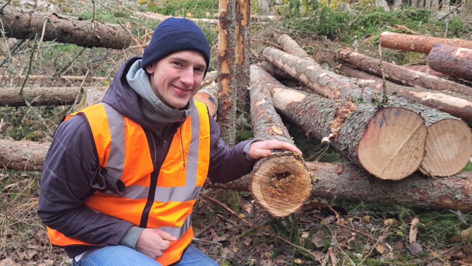 Isak sitting beside logs with rotrot. Photo. 